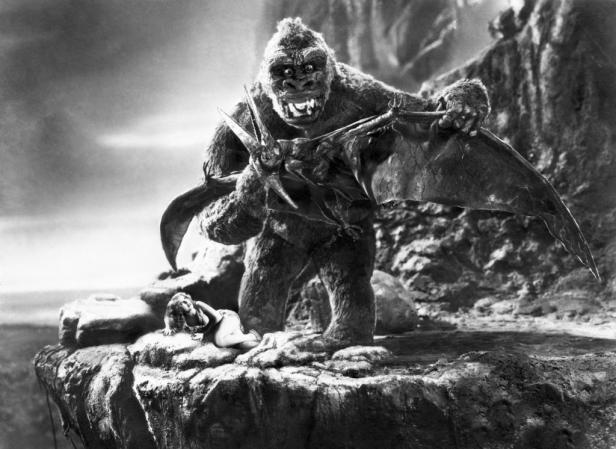 King Kong steht mit einem erlegten Flugsaurier über einer Frau auf einem Felsen.