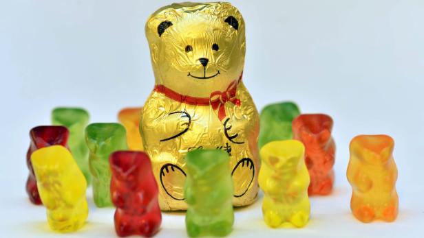 Ein goldener Schokoladenbär steht inmitten einer Gruppe von Gummibärchen.
