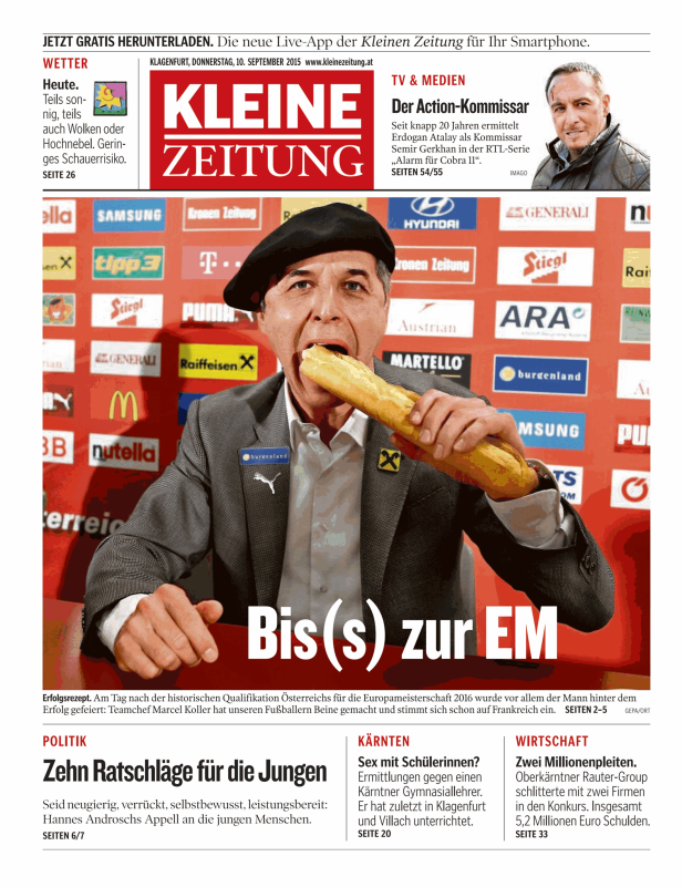 Ein Mann mit Baskenmütze isst ein Baguette vor einer Wand mit Sponsorenlogos.