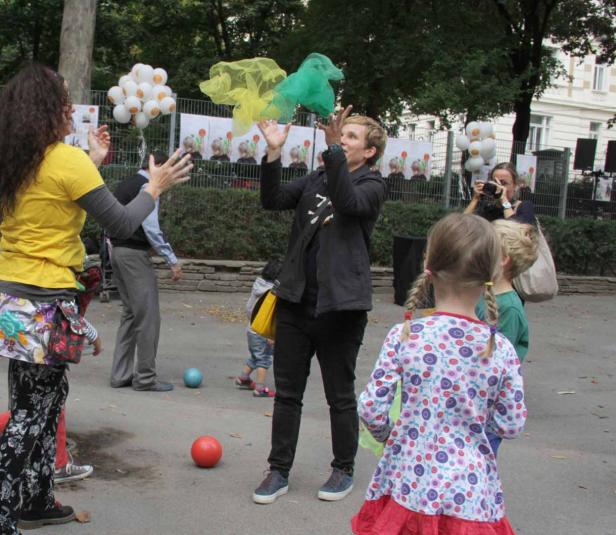Eine Frau wirft gelbe und grüne Tücher in die Luft, während Kinder zusehen.