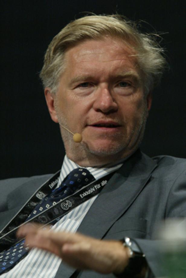 Ein Mann mit blondem Haar und Anzug spricht in ein Mikrofon.