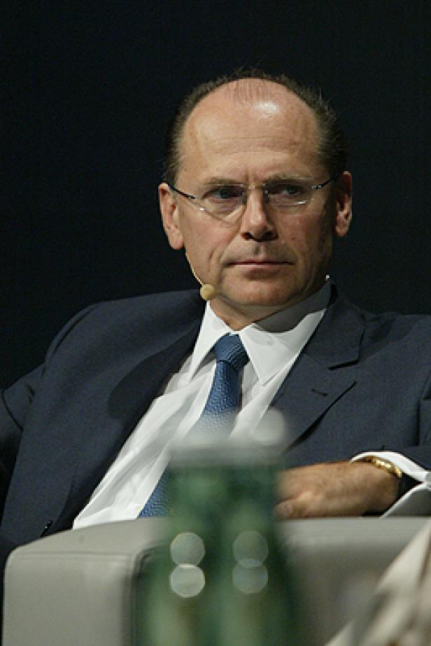 Ein Mann mit Brille und Anzug sitzt auf einem Podium.