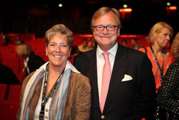 Eine Frau mit brauner Jacke und ein Mann mit Anzug posieren für ein Foto.