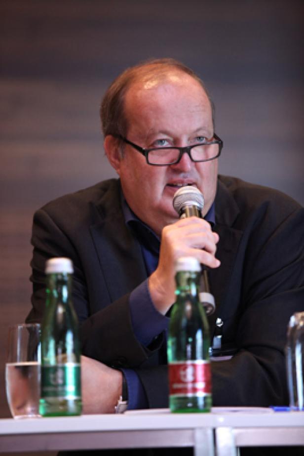 Ein Mann mit Brille spricht in ein Mikrofon auf einer Konferenz.