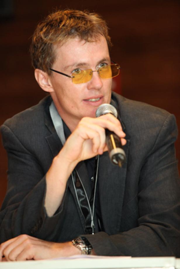 Ein Mann mit gelber Brille spricht in ein Mikrofon.