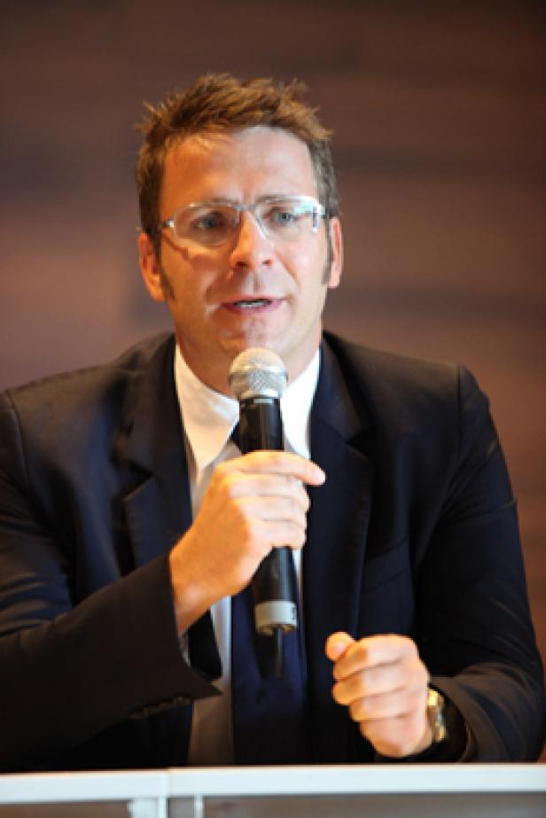 Ein Mann mit Brille und Anzug spricht in ein Mikrofon.