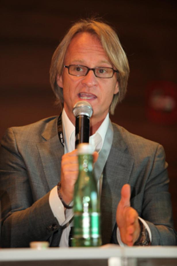 Ein Mann mit Brille und grauem Anzug spricht in ein Mikrofon.