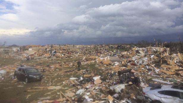 Ein zerstörtes Wohngebiet nach einem Tornado, mit Trümmern und beschädigten Fahrzeugen.