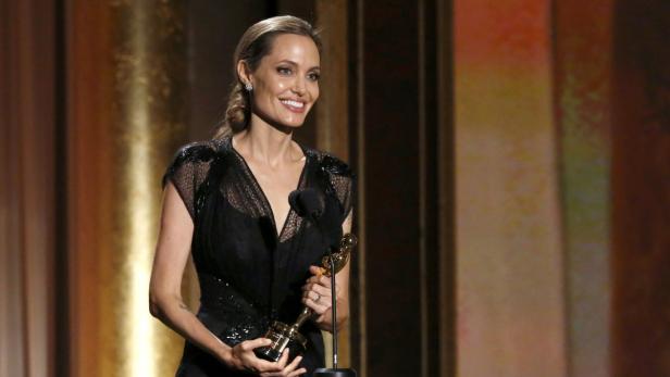 Angelina Jolie hält eine Auszeichnung in den Händen und lächelt.