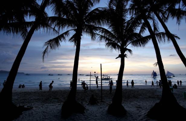 Menschen spielen Volleyball am Strand bei Sonnenuntergang, umrahmt von Palmen.