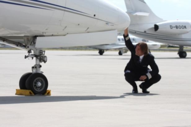 Ein Pilot hockt neben einem Privatjet und scheint ihn zu inspizieren.