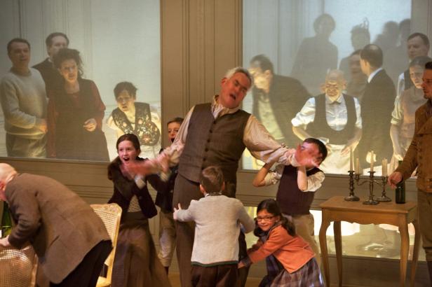 Eine Theaterszene mit einem Mann im Vordergrund, umgeben von aufgeregten Kindern.