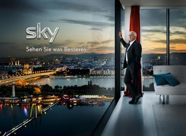 Ein Mann im Anzug blickt durch ein Fenster auf die abendliche Skyline von Wien.