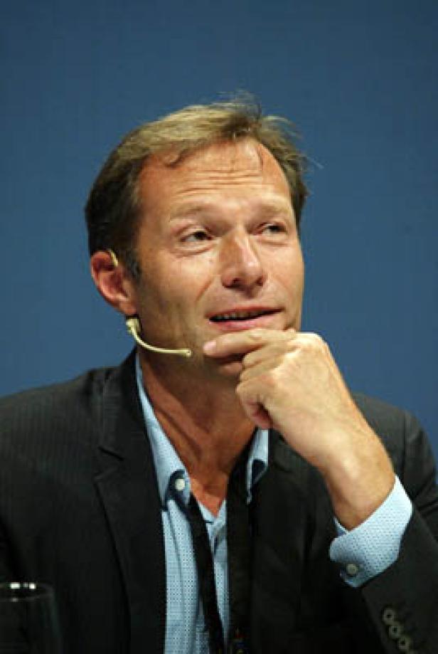 Ein Mann mit Mikrofon überlegt mit der Hand am Kinn.