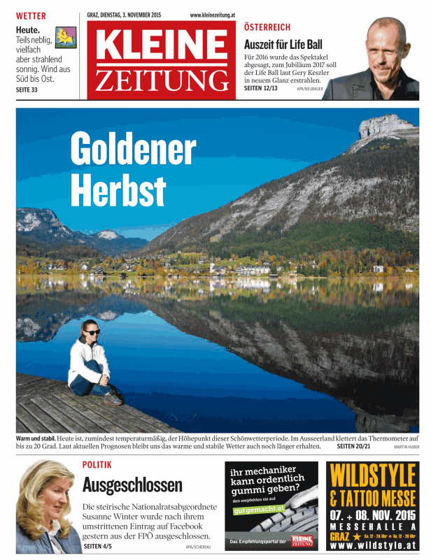Eine Frau sitzt am Ufer eines Sees vor einer Bergkulisse im goldenen Herbst.