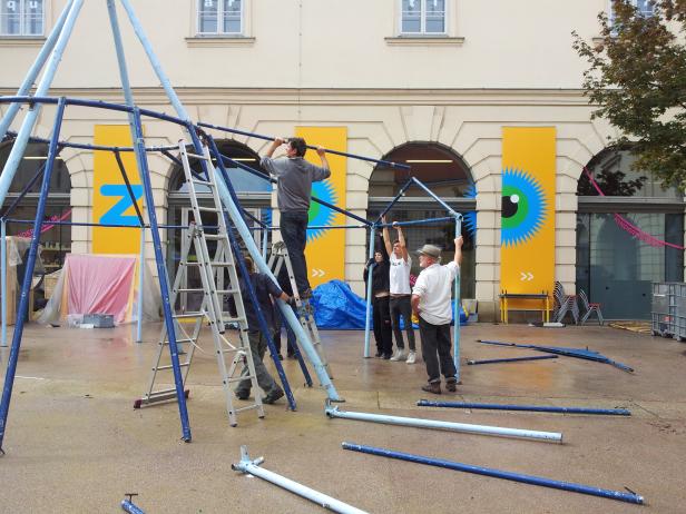 Mehrere Personen bauen eine blaue Metallkonstruktion im Freien auf.