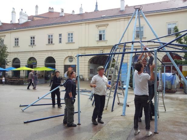 Mehrere Personen bauen eine blaue Metallkonstruktion im Freien auf.