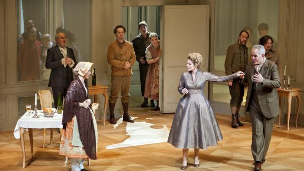 Eine Theaterszene mit mehreren Darstellern in historischen Kostümen auf einer Bühne.