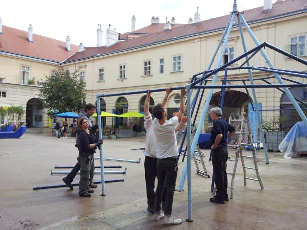 Mehrere Personen bauen eine blaue Metallkonstruktion in einem Innenhof auf.