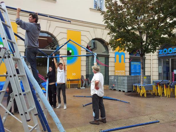Mitarbeiter bauen vor dem Zoom Kindermuseum eine blaue Rahmenkonstruktion auf.