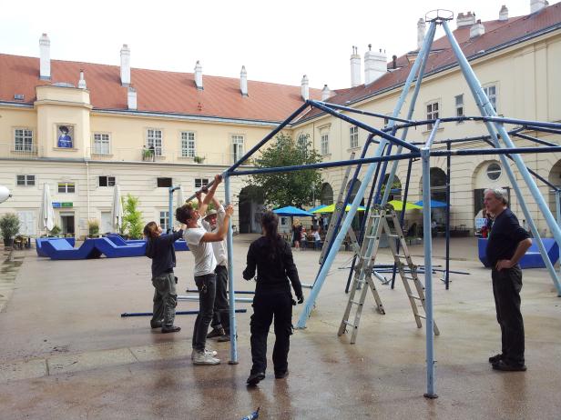 Eine Gruppe von Menschen montiert eine blaue Metallkonstruktion in einem Innenhof.