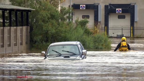 Ein Auto steht im Hochwasser, während ein Rettungshelfer durch das Wasser watet.