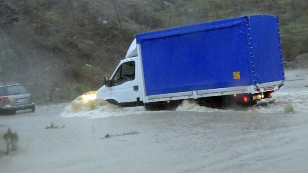 Ein weißer LKW mit blauer Plane fährt durch eine überflutete Straße.