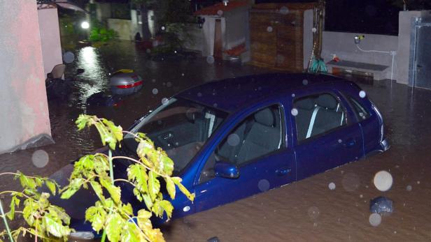 Ein blaues Auto steht im überfluteten Wasser einer Straße.