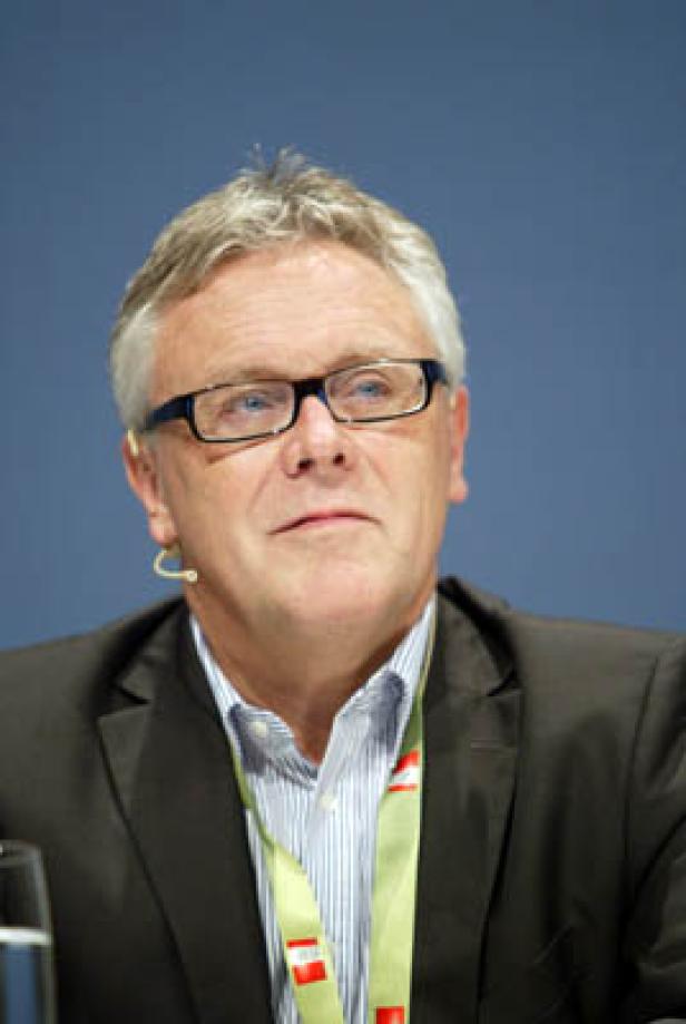 Ein Mann mit Brille und Anzug vor einem blauen Hintergrund.