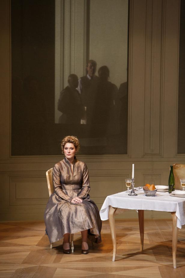 Eine Frau in einem Kleid sitzt an einem gedeckten Tisch in einem eleganten Raum.