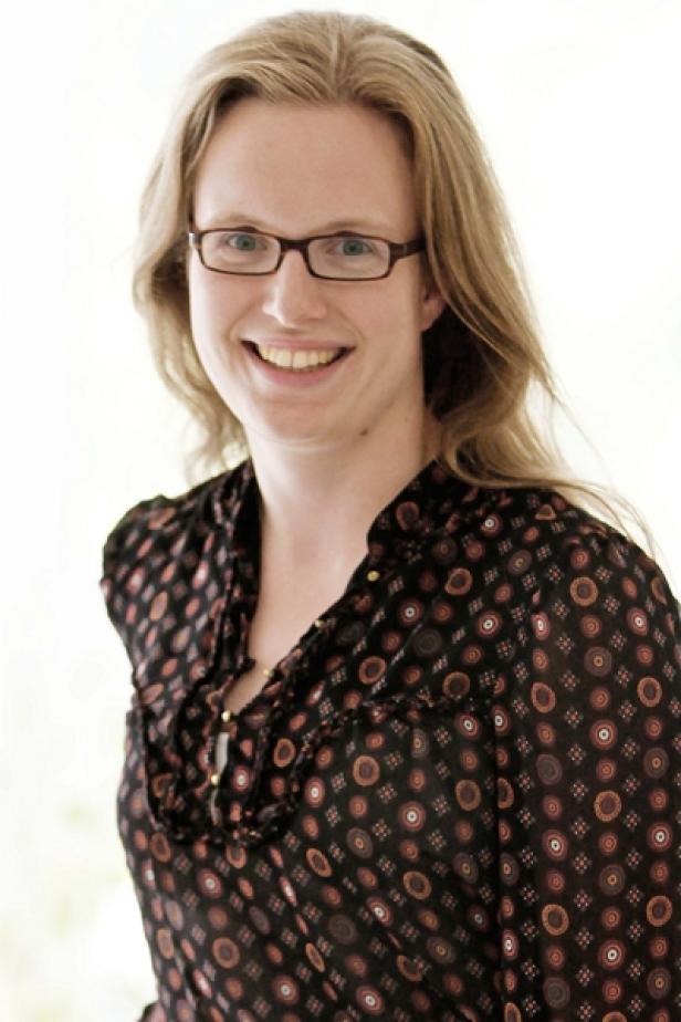 Eine lächelnde Frau mit Brille und gemusterter Bluse.