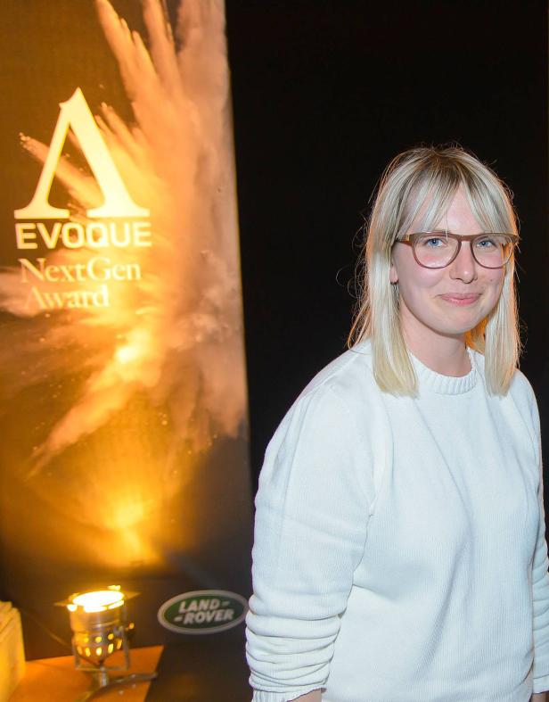Eine Frau steht vor einem Banner für den „EVOQUE NextGen Award“.