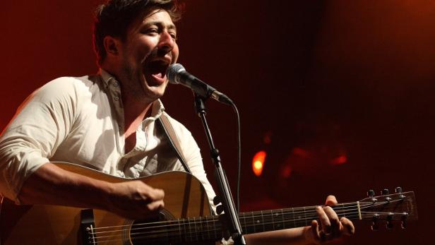 Ein Mann singt mit offenem Mund in ein Mikrofon und spielt Gitarre.