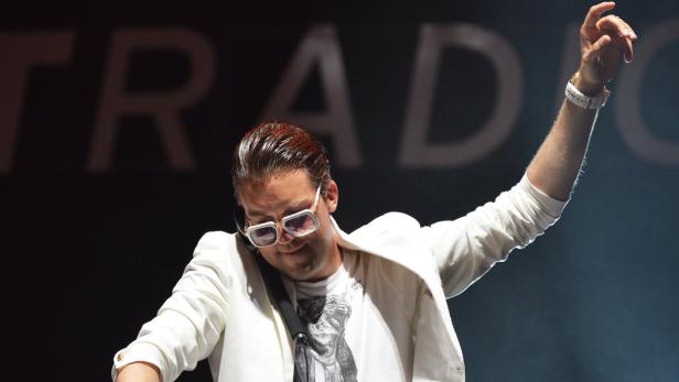 Ein Mann mit Sonnenbrille und weißem Anzug steht auf einer Bühne.