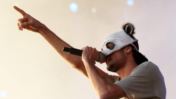 Ein Mann mit Pandamaske singt in ein Mikrofon und zeigt mit dem Finger nach oben.