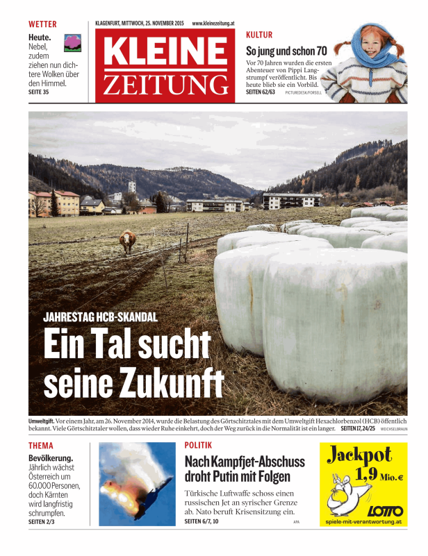 Eine ländliche Szene mit Feldern, Heuballen und Wohnhäusern vor bewaldeten Hügeln.