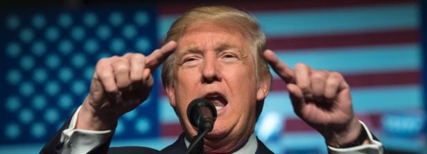 Donald Trump gestikuliert während einer Rede vor einer amerikanischen Flagge.
