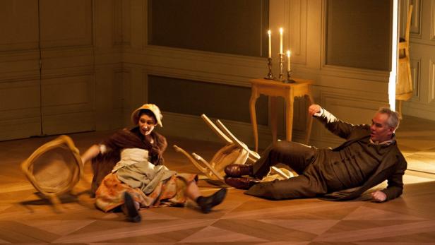 Eine Frau und ein Mann liegen auf dem Boden, um sie herum umgefallene Stühle.