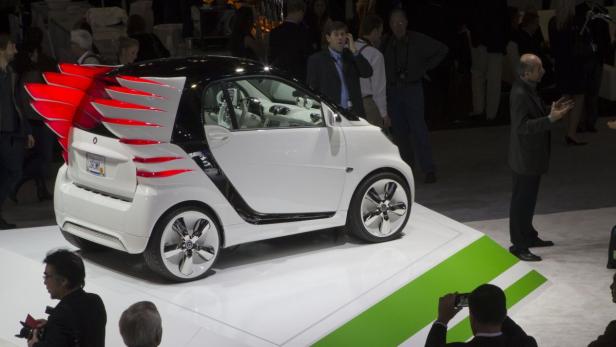 Ein weißer Smart mit roten, flügelartigen Aufsätzen steht auf einer Bühne.