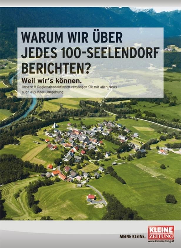 Luftaufnahme eines kleinen Dorfes in einer grünen Landschaft mit Bergen im Hintergrund.