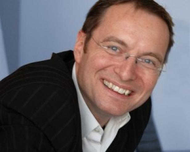 Wolfgang Bretschko, Vorstandssprecher Styria Media Group (c: styria mg) Ein lächelnder Mann mit Brille und Anzug vor einem blauen Hintergrund.