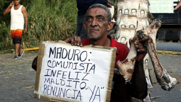 A man holds a bone and a placard that reads "Madur Venezuela: Bargeld-Engpass sorgt für Proteste und Plünderungen