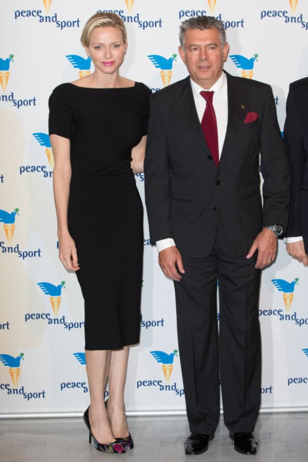 Fürstin Charlène von Monaco und ein Mann im Anzug posieren vor einem „Peace and Sport“-Hintergrund.