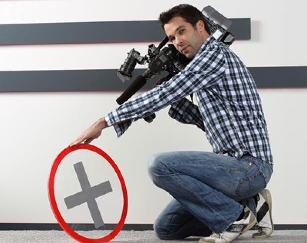 Robert Feitzinger, Filmemacher, Kamera-Mann, Cutter Salzburg Plus (c: salzburg plus/roithner) Ein Kameramann hockt neben einem runden Schild mit einem Pluszeichen.