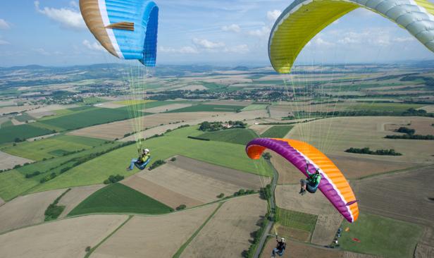 Mehrere Gleitschirmflieger schweben über einer ländlichen Gegend.