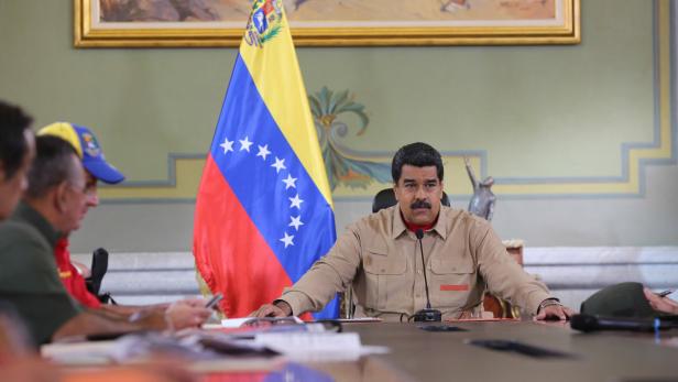Nicolás Maduro sitzt an einem Tisch vor der venezolanischen Flagge.