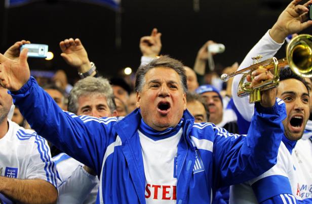 Jubelnde griechische Fans mit Trompete und Handys feiern.