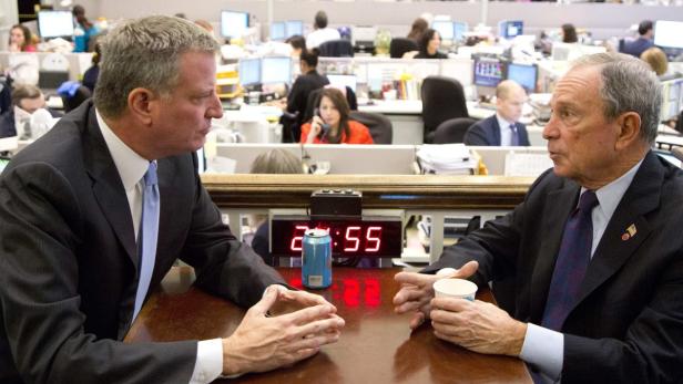 Bill de Blasio und Michael Bloomberg sitzen an einem Tisch und unterhalten sich.