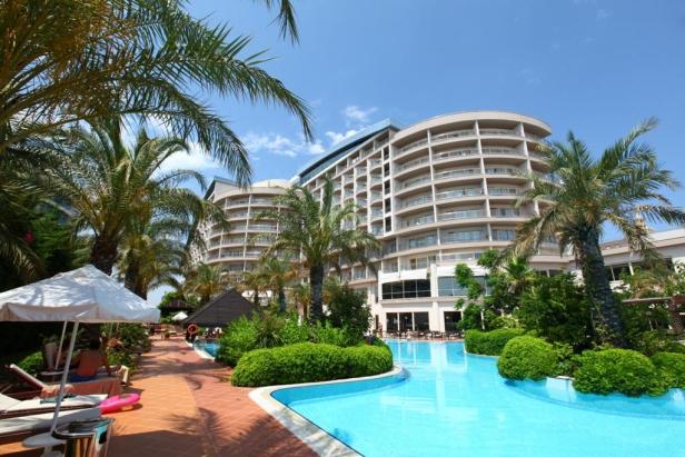 Ein großes Hotel mit Pool und Palmen an einem sonnigen Tag.