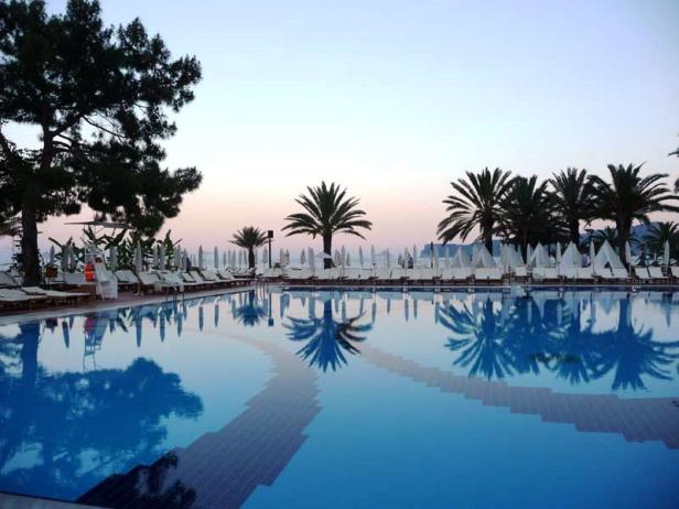 Ein Schwimmbecken spiegelt Palmen und Liegestühle bei Dämmerung wider.